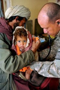 Young girl being held by her father while being treated by an American army medical staff member