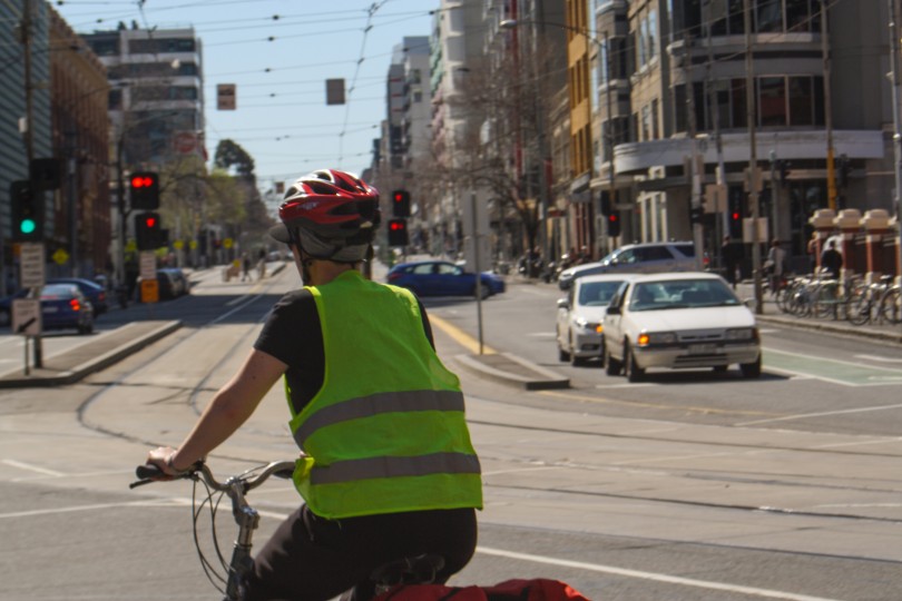 A cyclist in a high-vis vest rides on a street with cars in the background