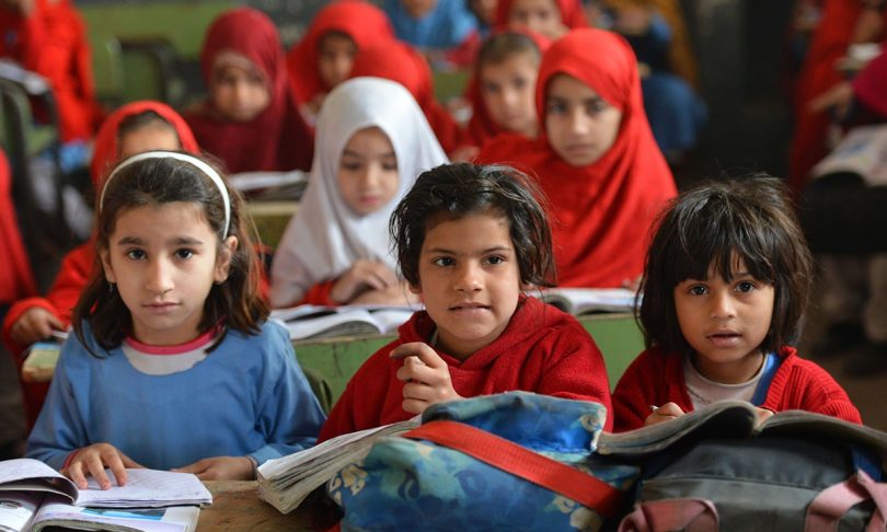Three children sitting in a classroom in Pakistan.