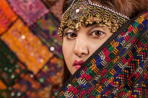 Close up of Pakistani woman dressed in traditional head-dress and colourful clothing.