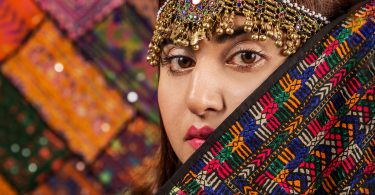 Close up of Pakistani woman dressed in traditional head-dress and colourful clothing.