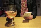 Anonymous person with large glass of white wine in one hand and peering at phone in the other.