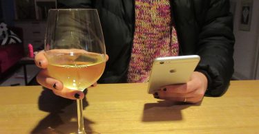 Anonymous person with large glass of white wine in one hand and peering at phone in the other.