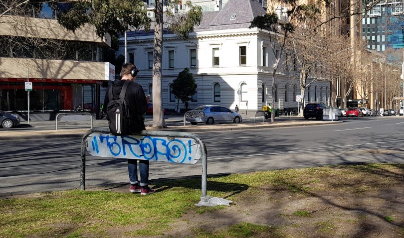 Anonymous youth sitting on graffitied road sign