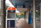 A Telstra public payphone booth opposite a milkbar on a suburban strip